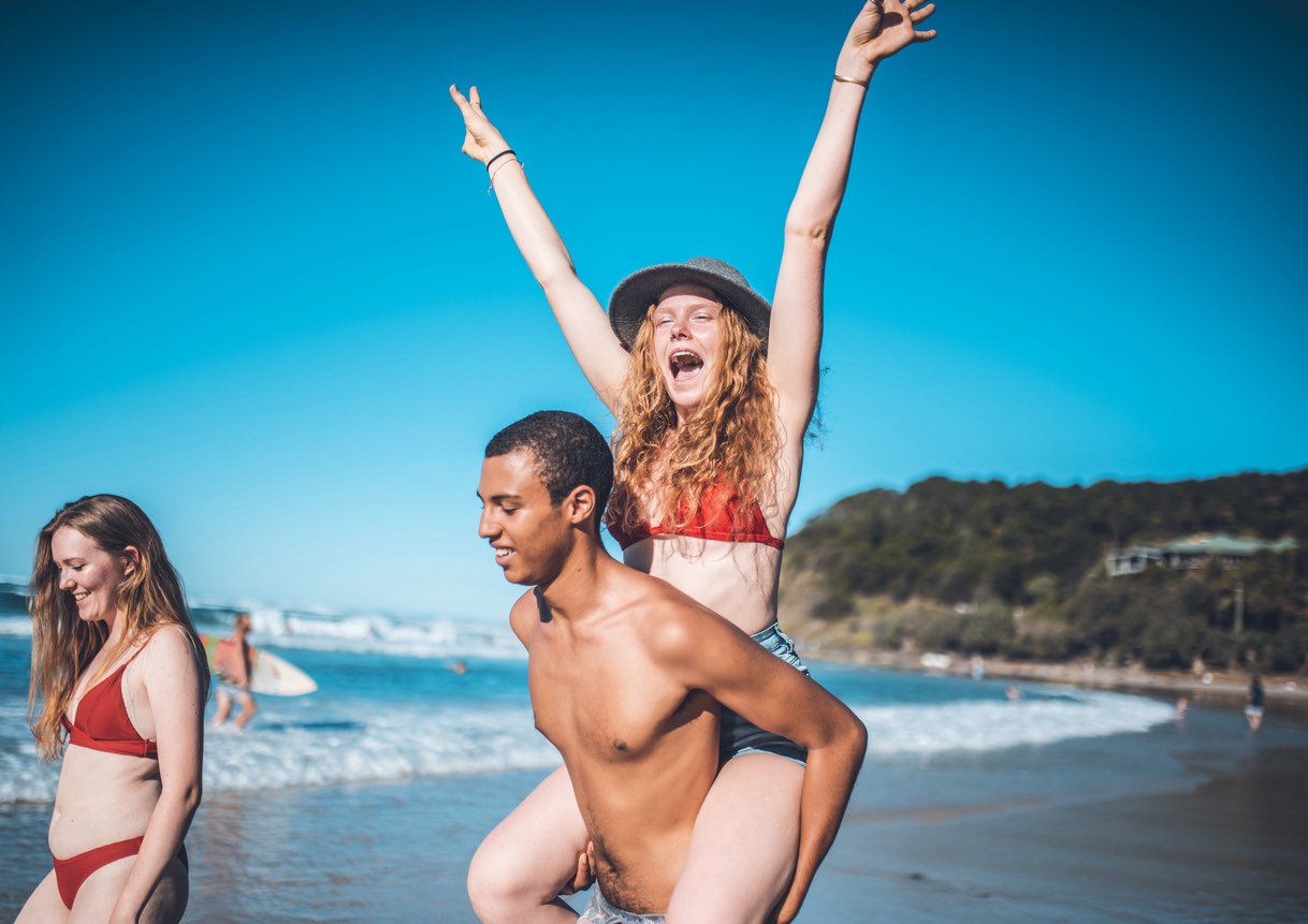 Boyfriend is piggybacking his girlfriend on the beach at Byron Bay .