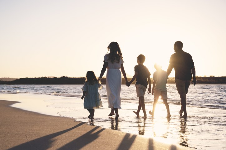 Mother and Father with 3 kids holding hands walking along the waters edge with the sunset in Noosa