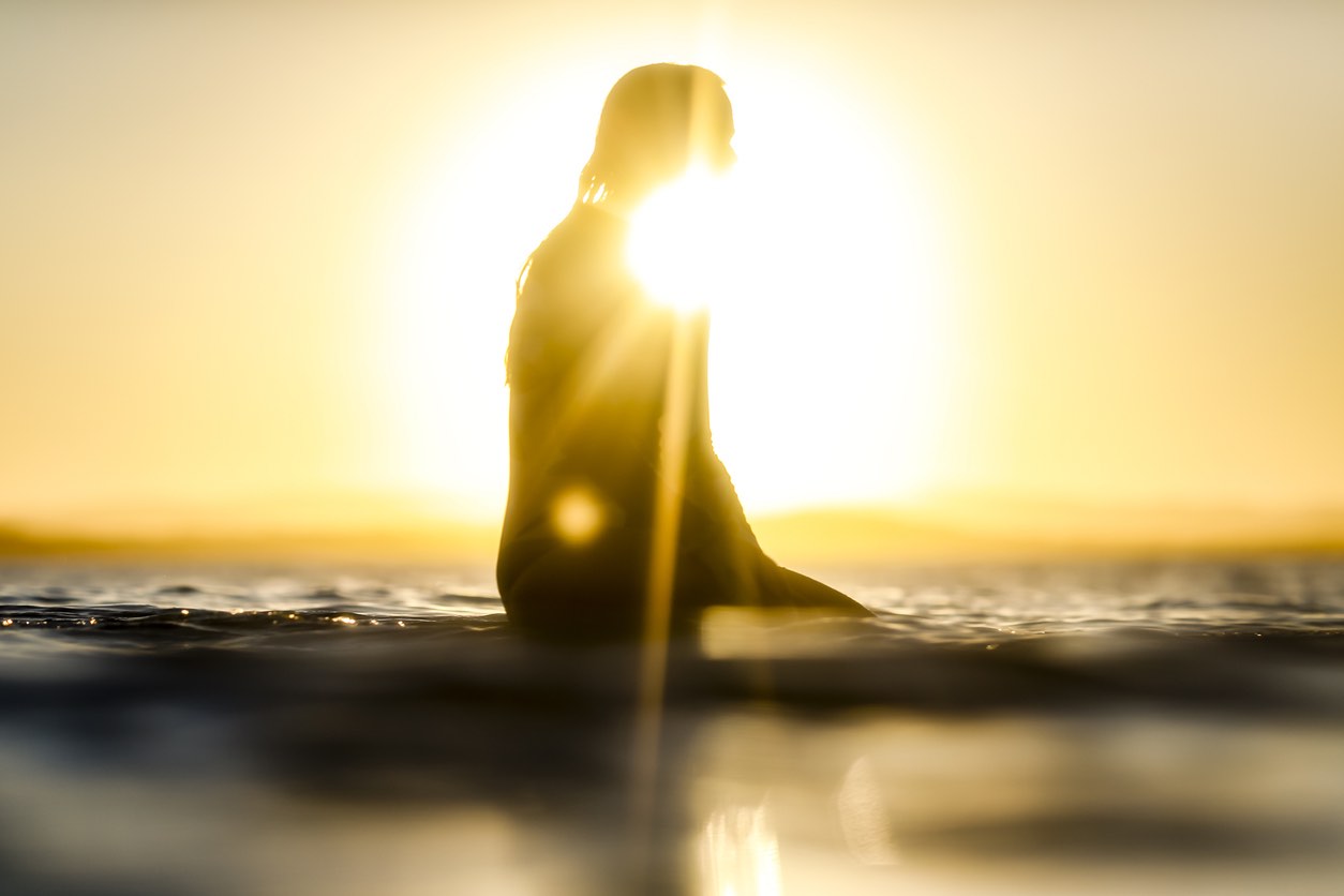 A female surfer silhouetted by the setting sun on the horizon over the ocean at tea Tree Bay, Noosa National Park.